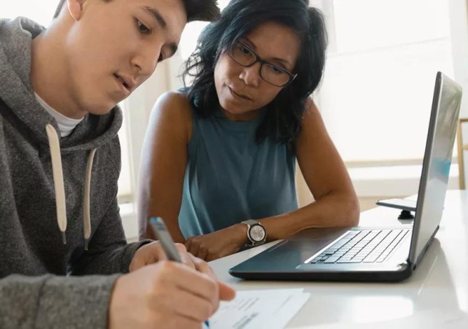 Photo of a mother and son sitting in front of a laptop and reviewing options for paying for college.